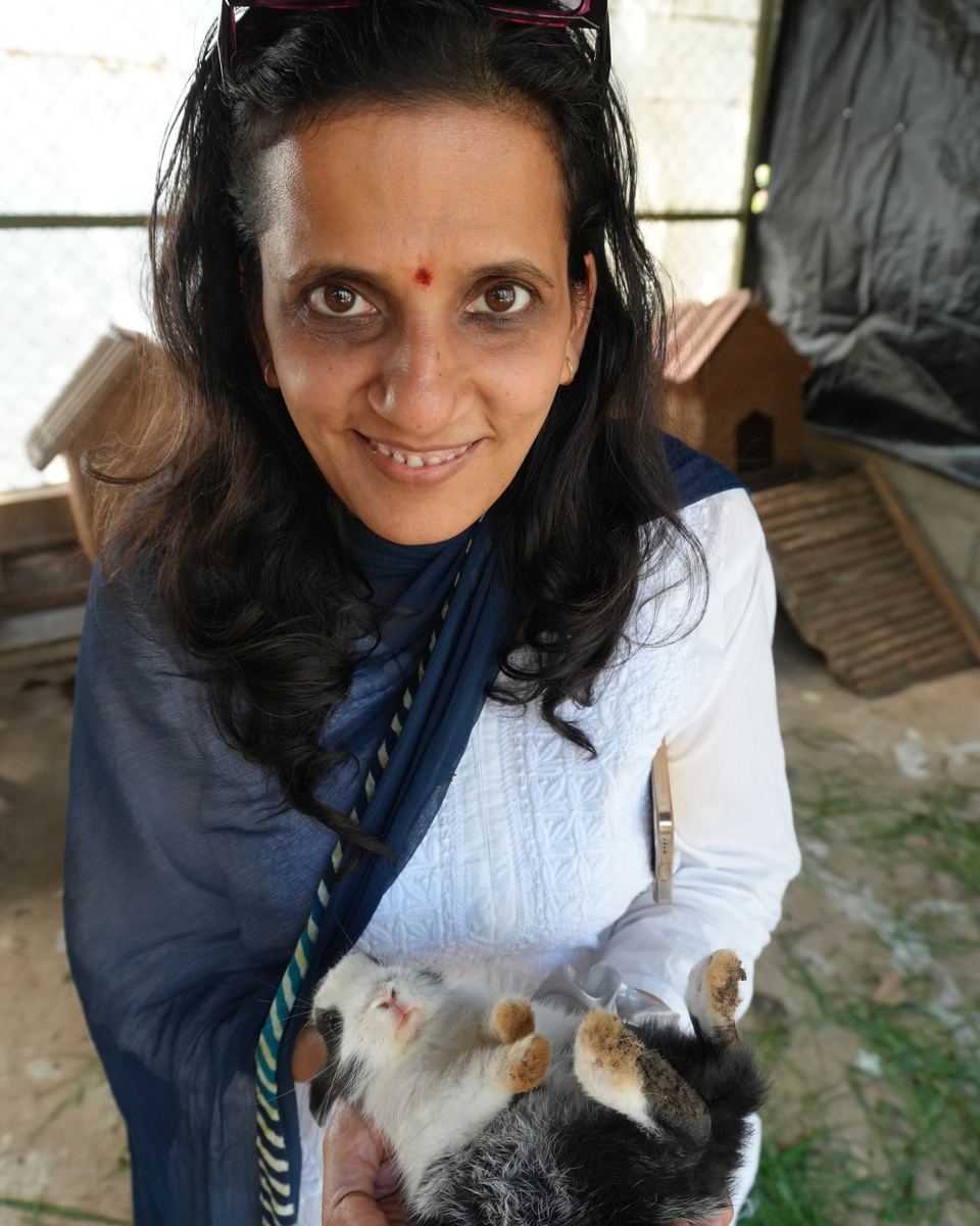 Ritu outdoors among plants, smiling and holding a white rabbit
